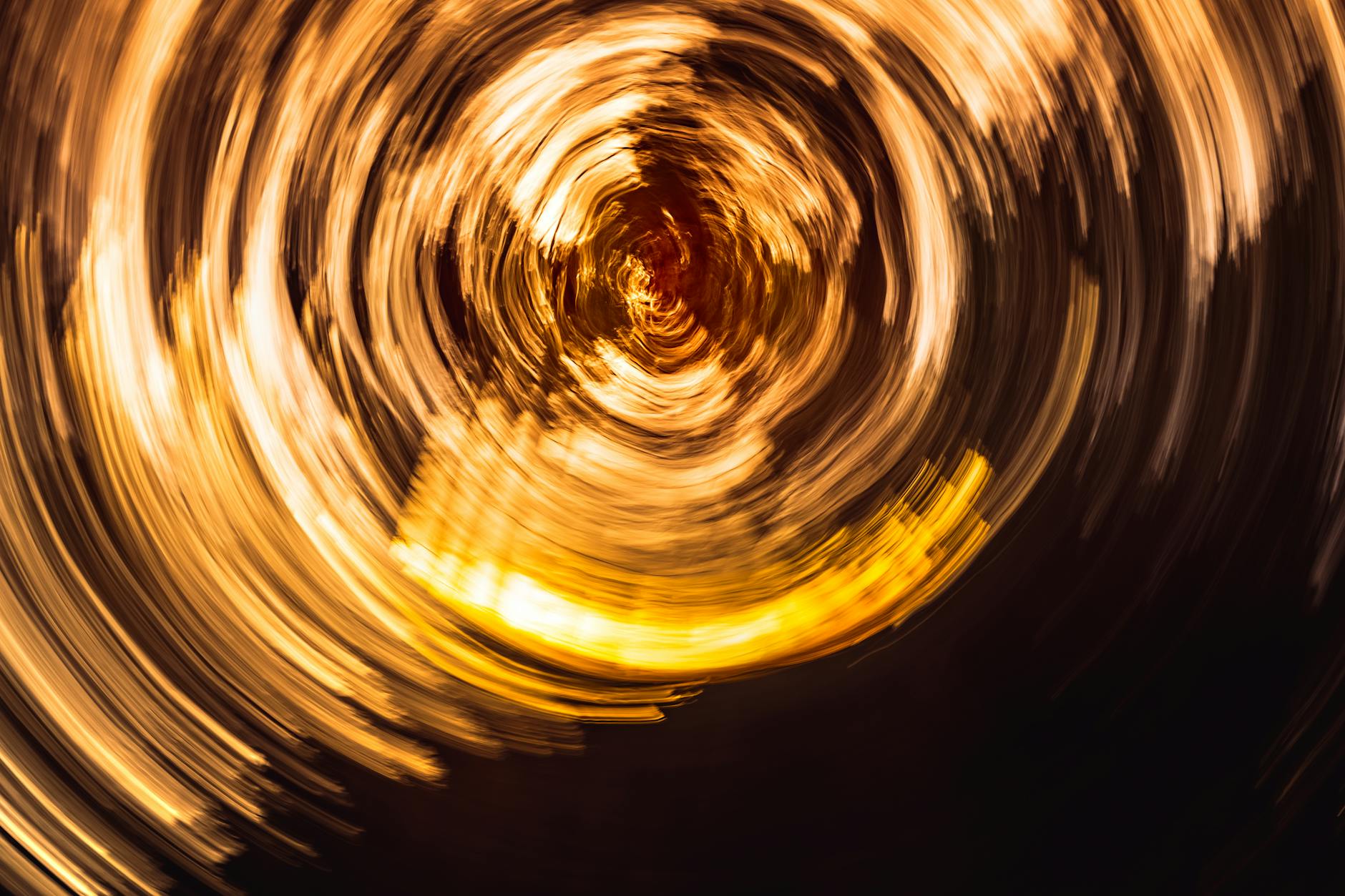 A vibrant abstract swirl of golden and orange light creating a visual vortex effect.