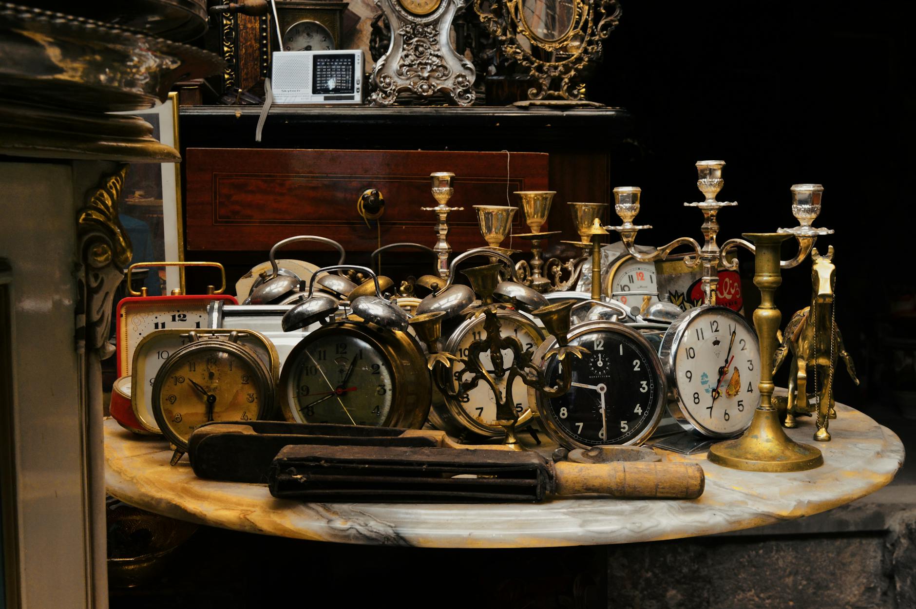 A collection of vintage alarm clocks and candlesticks on a marble table in a rustic setting.