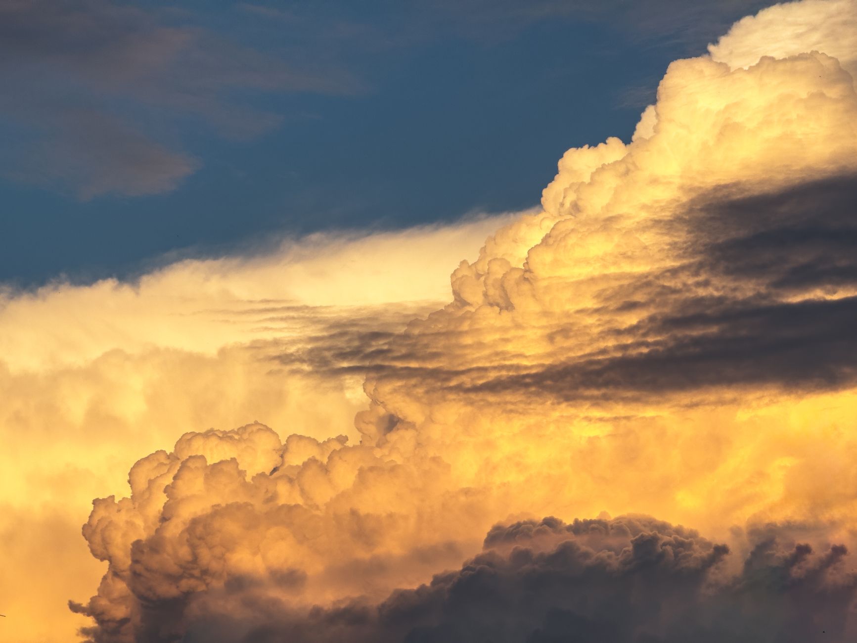 Sunset view of dramatic cumulonimbus clouds illuminated in gold hues against a darkening sky.