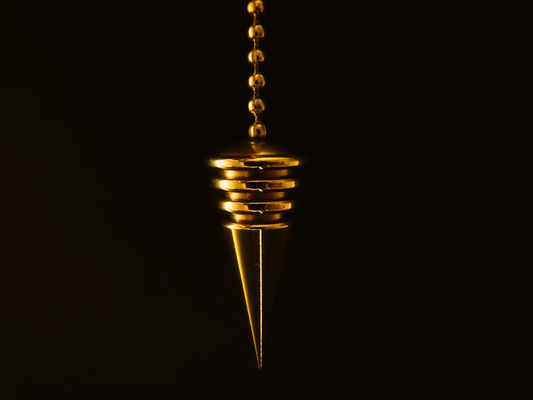An elegant gold pendulum with chain on a mysterious black background.